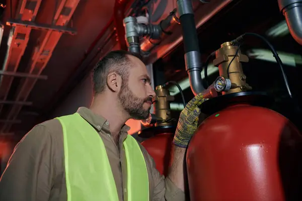 Técnico enfocado bien parecido en ropa de seguridad comprobar cilindros de gas durante el trabajo, centro de datos - foto de stock