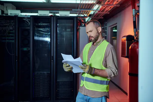 Focused gray hired specialist in safety clothes looking attentively at his paperwork, data center — Stock Photo