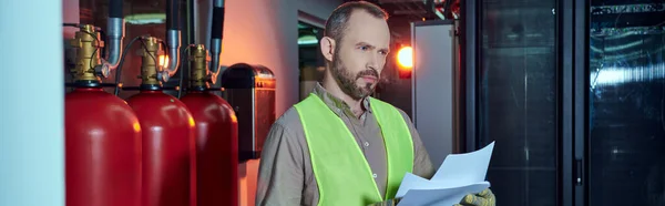 Concentrated bearded man in safety vest holding papers and looking away, data center, banner — Stock Photo