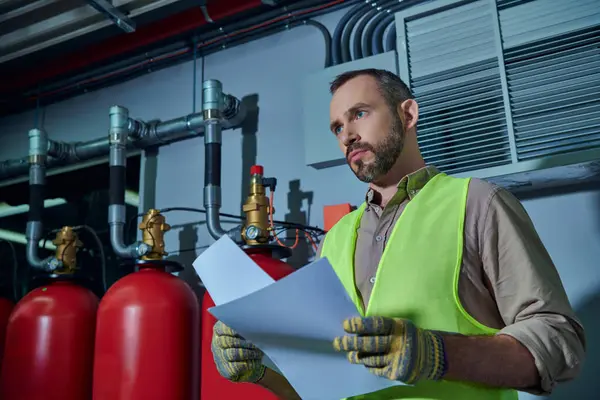 Good looking pensive technician in safety vest holding paperwork and looking away, data center — Stock Photo