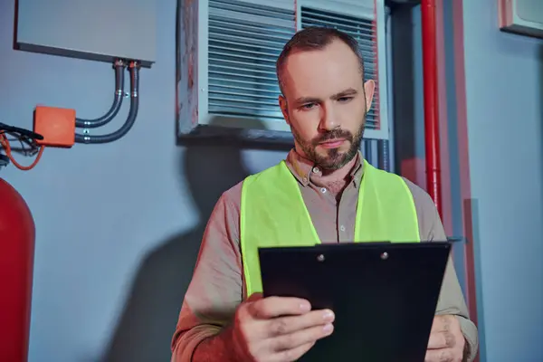 Attractive pensive professional in safety vest looking at clipboard while working in data center — Stock Photo