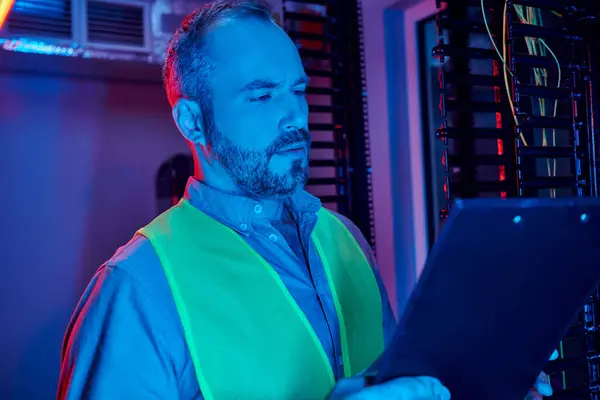 Concentrated specialist in safety clothes with beard looking at clipboard while working hard — Stock Photo