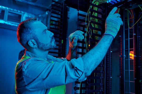 Good looking concentrated technician in safety gloves and vest inspecting cables, data center — Stock Photo