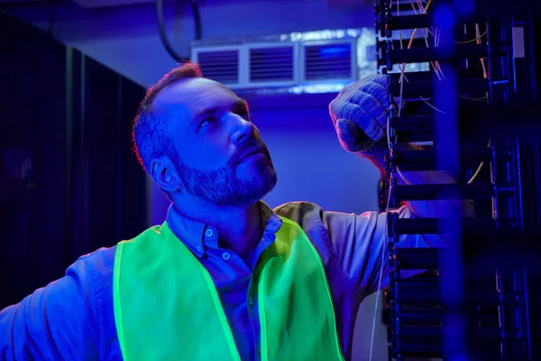 Hardworking jolly specialist in safety vest and gloves inspecting information center, data storage — Stock Photo