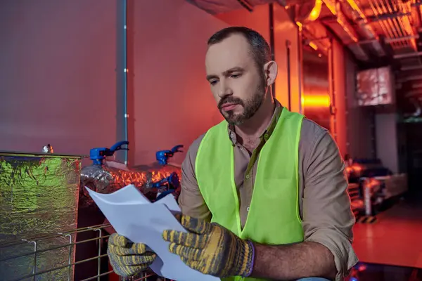 Handsome concentrated technician in safety clothes looking attentively at paperwork, data center — Stock Photo