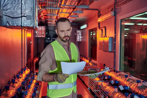 Concentrated hardworking man in safety clothes looking attentively at his paperwork, data center — Stock Photo