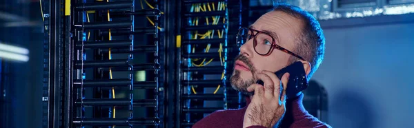 Concentrated professional in turtleneck with glasses and beard talking by phone, data center — Stock Photo