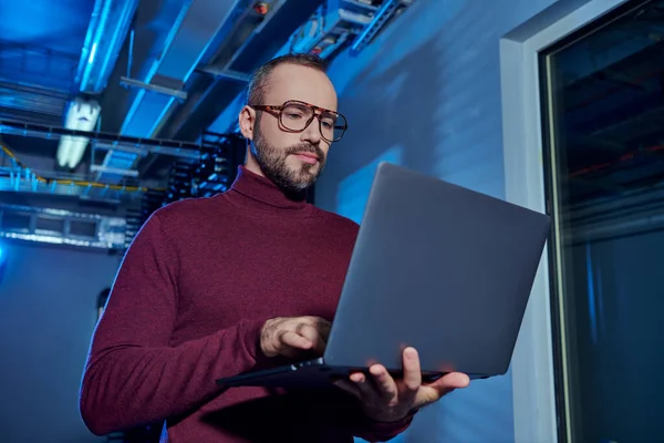 Pensive jolly data center specialist in turtleneck with beard and glasses working hard on his laptop — Stock Photo