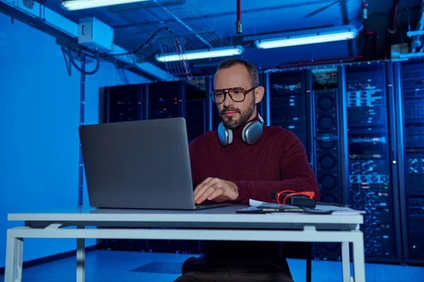 Jolly good looking data center specialist in turtleneck with headphones working on his laptop — Stock Photo