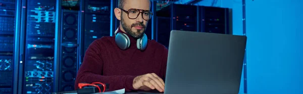 Focused joyful specialist in turtleneck with headphones working on his laptop, data center, banner — Stock Photo