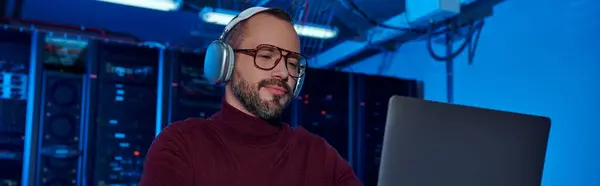 Fröhlicher Spezialist für Rollkragenpullover mit Kopfhörern, der hart an seinem Laptop, Rechenzentrum, Banner arbeitet — Stockfoto