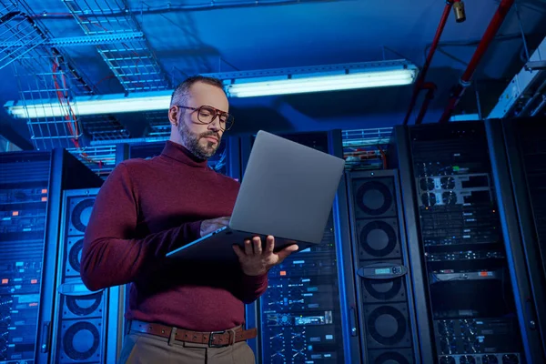 Bello specialista di data center laborioso in dolcevita guardando attentamente il suo computer portatile — Foto stock