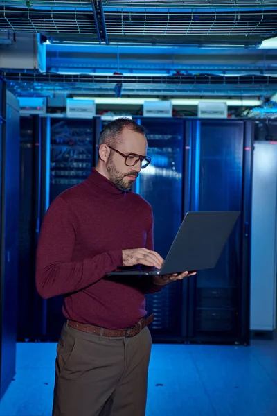 Pensive good looking data center specialist in turtleneck with glasses working on his laptop — Stock Photo