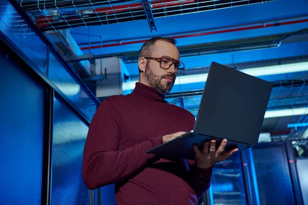 Concentrated handsome specialist with beard and glasses in turtleneck working hard on his laptop — Stock Photo