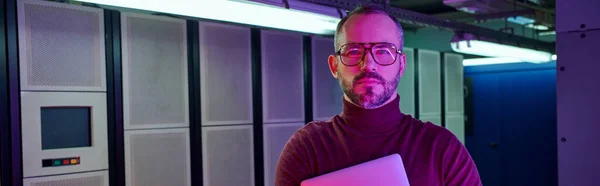 Pensive specialist in turtleneck holding laptop and looking at camera, data center, banner — Stock Photo