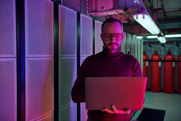 Joyous attractive professional in turtleneck looking at his laptop and smiling happily, data center — Stock Photo