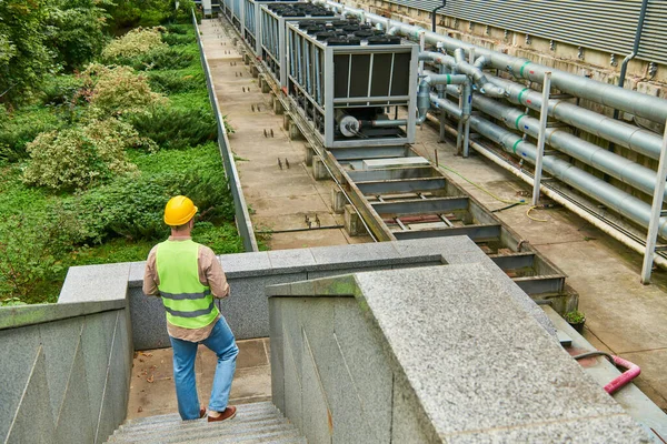Back view of dedicated professional in helmet and safety vest standing outside of data center — Stock Photo