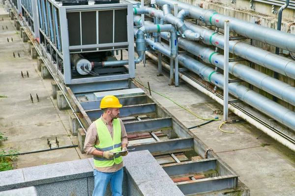 Handsome focused technician in safety vest and helmet posing with clipboard outside, data center — Stock Photo