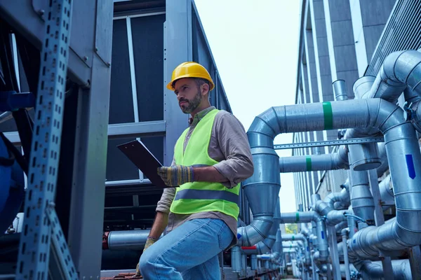 Attractive concentrated technician in safety vest holding clipboard while working outside, data — Stock Photo
