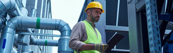Focused technician in safety vest holding clipboard while working outside, data center, banner — Stock Photo