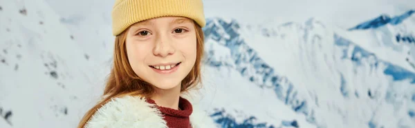 Trendy little girl in warm stylish outfit smiling at camera with mountain backdrop, fashion, banner — Stock Photo