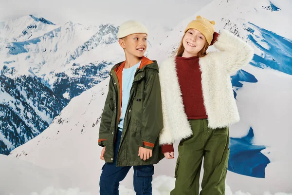 Pequeño niño mirando a linda chica, ambos vistiendo trajes cálidos de invierno y sonriendo alegremente, moda - foto de stock