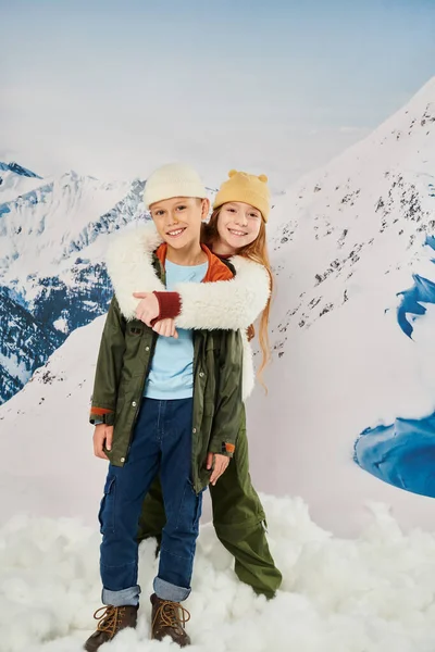 Tiro vertical de pequeños amigos en trajes de invierno abrazando y sonriendo a la cámara, concepto de moda - foto de stock