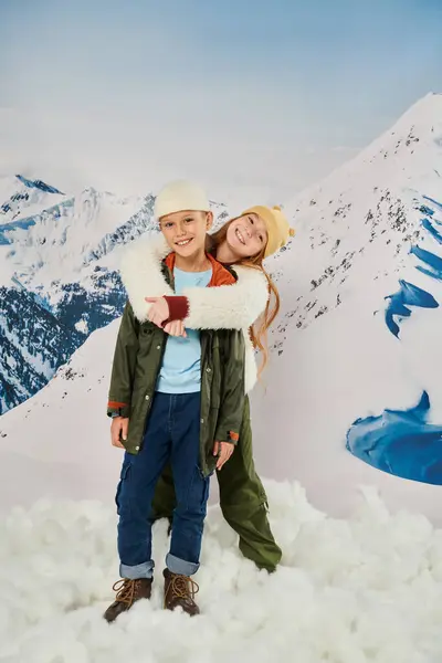 Вертикальный снимок веселых маленьких друзей в зимнем наряде, улыбающихся в камеру и обнимающихся тепло, мода — стоковое фото