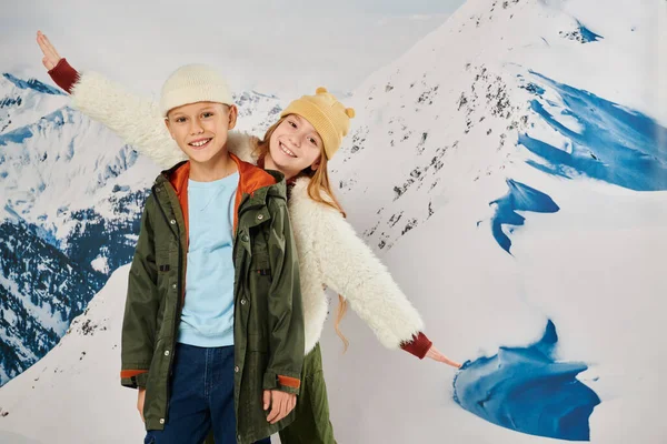 Cheerful little boy and girl with beanie hats having fun with snowy mountain on backdrop, fashion — Stock Photo