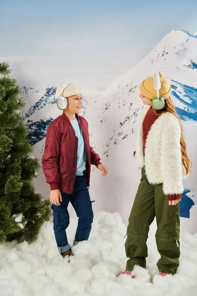 Vertical shot of little friends in stylish warm jackets with headsets smiling at each other, fashion — Stock Photo