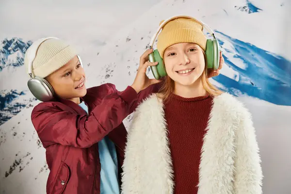 Jolly preadolescent children in warm trendy attires with headphones with mountain backdrop, fashion — Stock Photo
