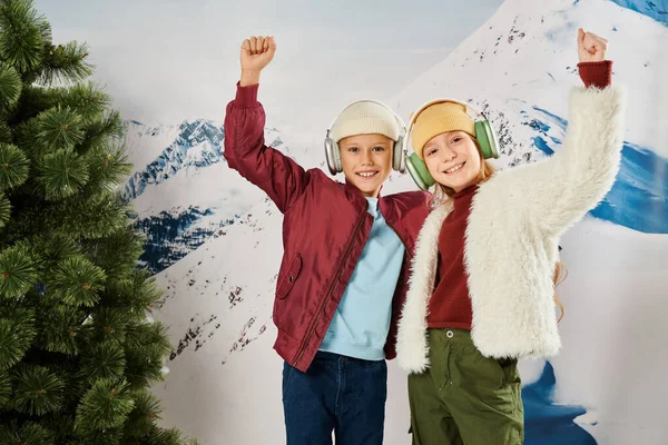 Joyous little children in stylish jackets cheering with raised arms smiling at camera, fashion — Stock Photo