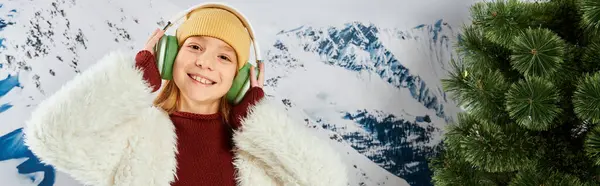 Alegre chica de moda en traje cálido escuchando música en los auriculares y sonriendo alegremente, moda, bandera - foto de stock