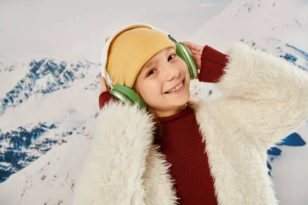 Ritratto di allegra preadolescente in cappello beanie con auricolare sorridente alla macchina fotografica, concetto di moda — Foto stock