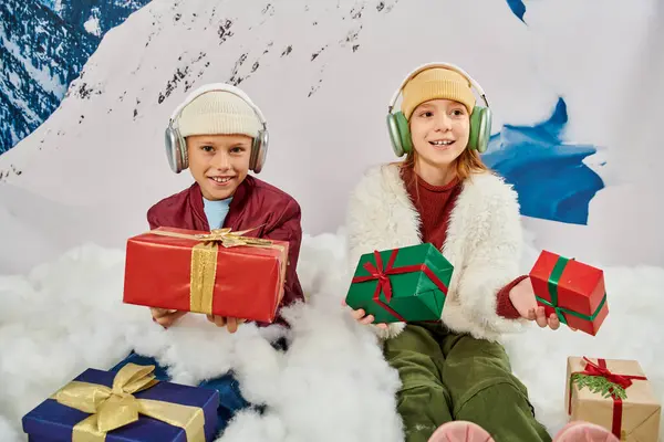 Preteen adorable children with headphones and presents sitting on snow, smiling at camera, fashion — Stock Photo
