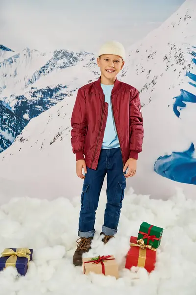 Vertical shot of preteen boy in red stylish jacket posing next to presents and smiling at camera — Stock Photo
