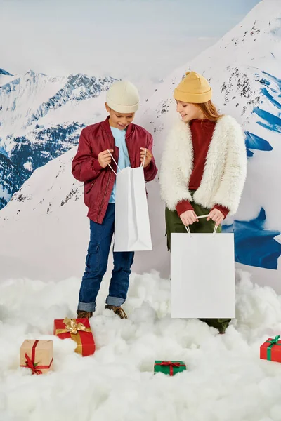 Vertical shot of little friends in stylish winter clothes looking inside of present bag, fashion — Stock Photo