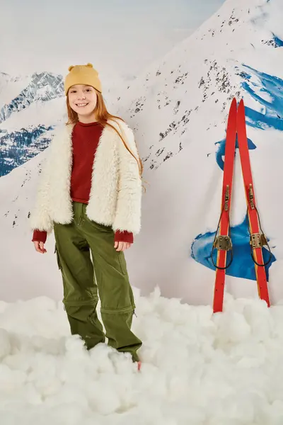 Colpo verticale di jolly preteen girl in abbigliamento caldo alla moda in posa con gli sci sullo sfondo, moda — Foto stock