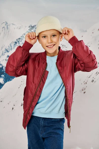 Вертикальный снимок preadolescent мальчика в стильной красной куртке надевая шапку шапочки, концепция моды — стоковое фото