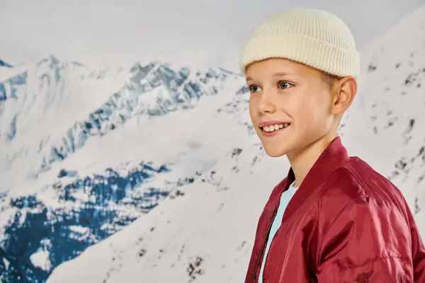 Retrato de niño preadolescente alegre en gorro sombrero mirando hacia otro lado con la montaña nevada en el telón de fondo, la moda - foto de stock