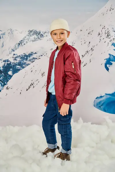 Vertical shot of little boy in stylish warm clothes standing on snow and smiling at camera, fashion — Stock Photo