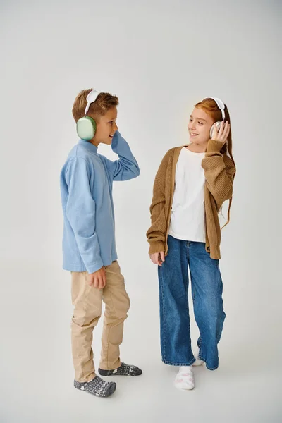 Alegre preadolescente amigos posando con auriculares en gris telón de fondo sonriendo el uno al otro, la moda — Stock Photo