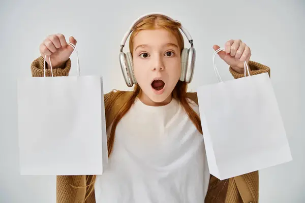 Astonished little girl with headphones showing present bags at camera, Black Friday, fashion concept — Stock Photo
