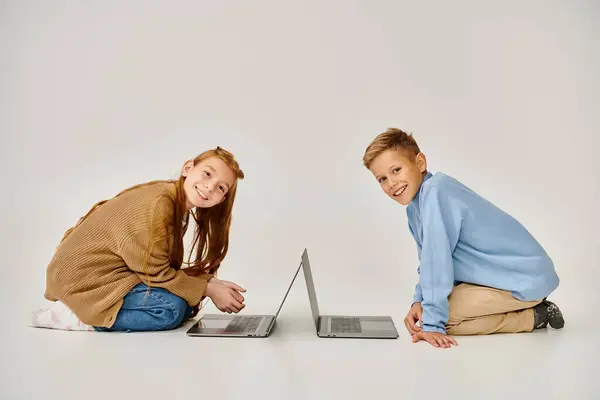 Alegre preadolescente amigos en ropa de invierno en el suelo con ordenadores portátiles sonriendo a la cámara, concepto de moda - foto de stock