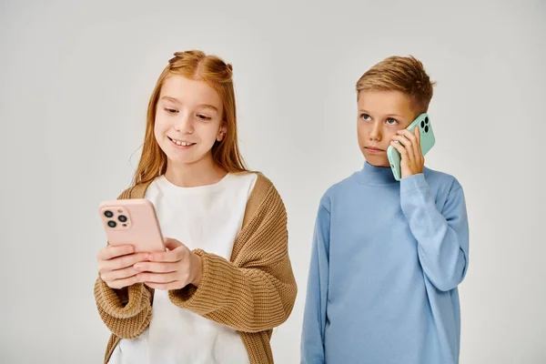 Fokussierter kleiner Junge telefoniert in der Nähe seiner fröhlichen Freundin und schaut auf ihr Handy, Modekonzept — Stockfoto