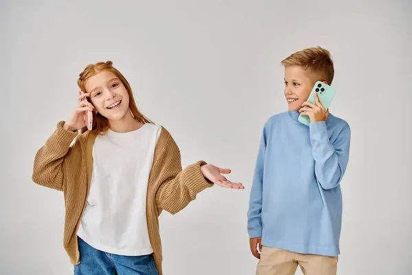 Enfants préadolescents joyeux en tenues décontractées élégantes parler par téléphone sur fond gris, la mode — Photo de stock