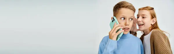 Chocado pré-adolescente menino falando por telefone enquanto seu alegre par sussurrando algo em seu ouvido, banner — Fotografia de Stock