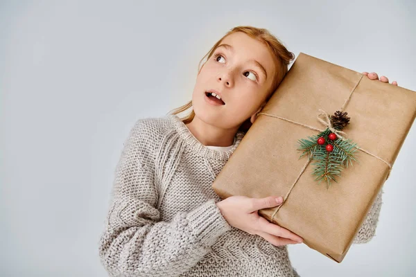 Überrascht kleines Mädchen in lässiger Winterkleidung posiert mit Geschenk und schaut weg, Mode — Stockfoto