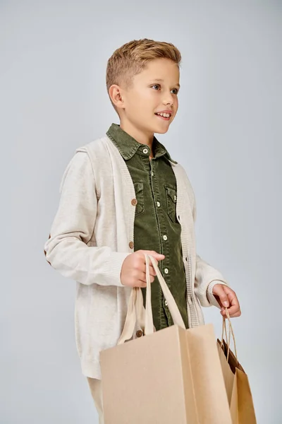 Vertical shot in profile of preteen cute boy in casual attire holding present bags, fashion concept — Stock Photo