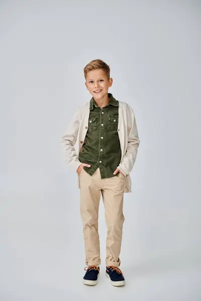 Vertical shot of preteen little boy in casual outfit on gray backdrop with hands in pockets, fashion — Stock Photo